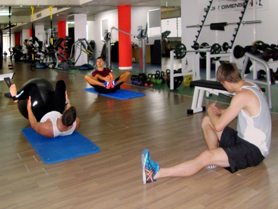 Athletes performing floor exercises on mats with gym equipment in the background