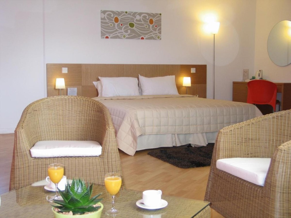 Spacious hotel room with double bed, wicker chairs, and coffee table with orange juice