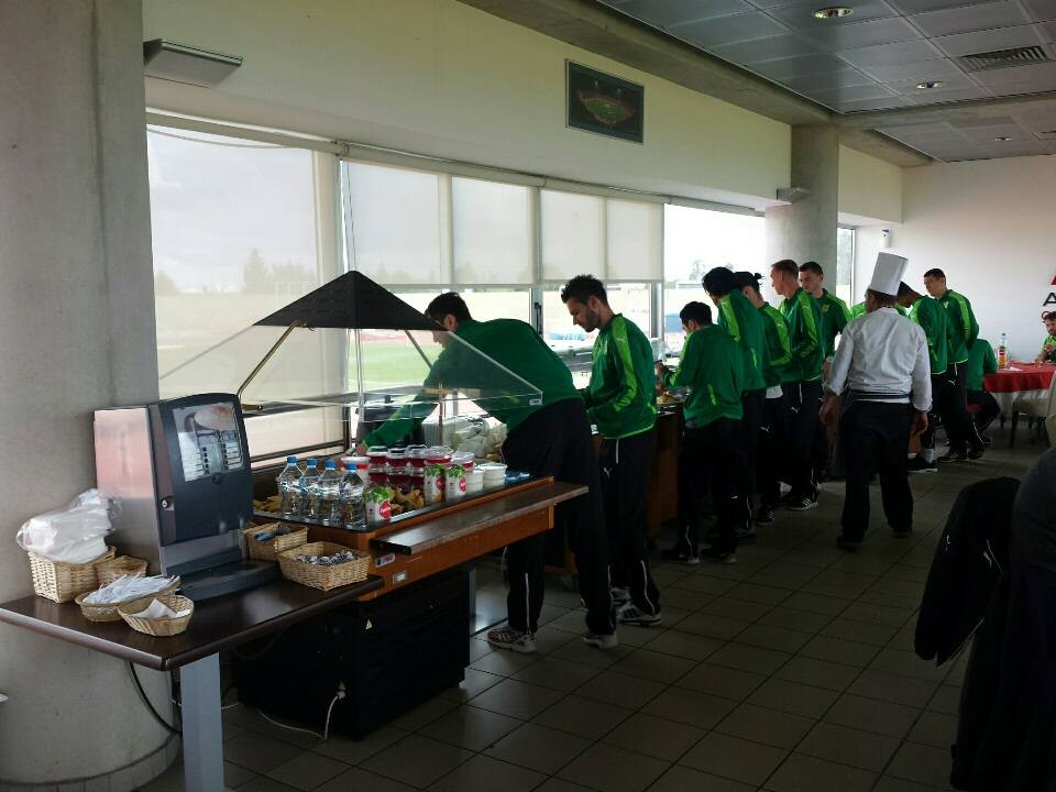 Athletes in green sportswear selecting meals from buffet during training camp dining