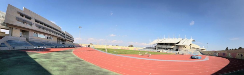 Panoramic view of athletics stadium with two grandstands and red running track for drills or races