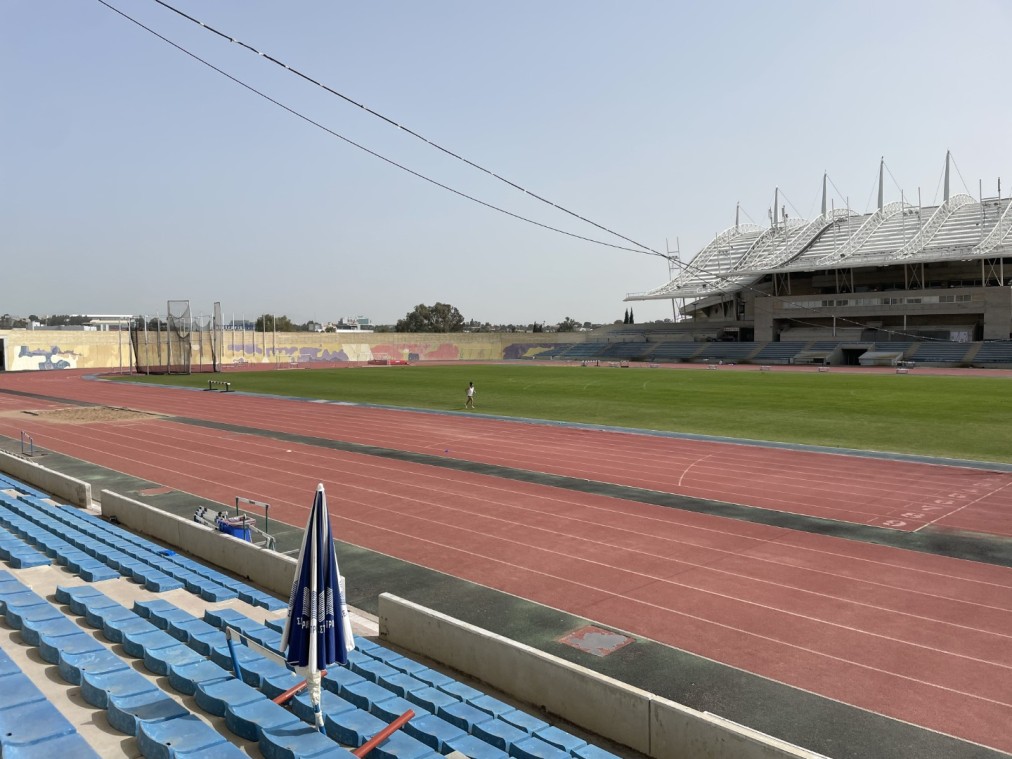 Athletics stadium with red running track, green field, and modern grandstand used for training camps and practice sessions