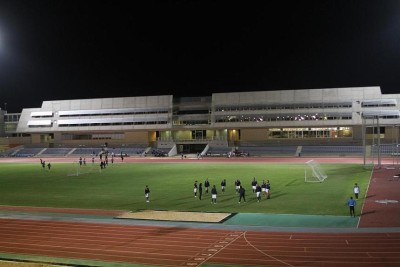Night practice session on a lit athletics field with players training near running track