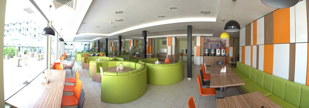Modern lounge with green seating, orange accents, and tables, a relaxation space during training camp downtime