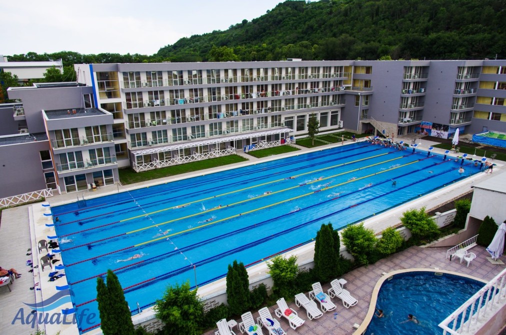 Elevated view of long outdoor swimming pool surrounded by hotel and loungers for training camp recovery