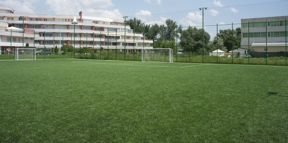 Green artificial turf soccer field with goalposts near buildings, used for training camp drills