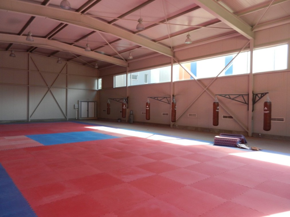 Indoor gym hall with red mat flooring and wall pads, ready for practice sessions