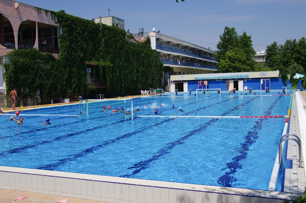 Swimmers practicing laps in an outdoor pool with lane ropes, part of a training camp workout