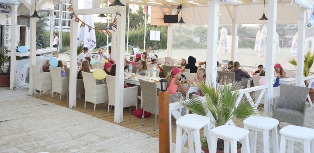 Outdoor covered dining terrace with white furniture and guests, serving group meals during training camp