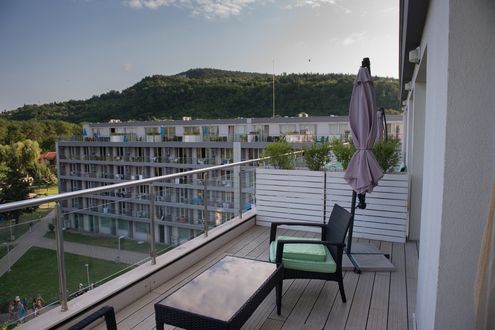 Hotel balcony with outdoor chairs and table overlooking buildings and greenery, athlete lodging during training camp