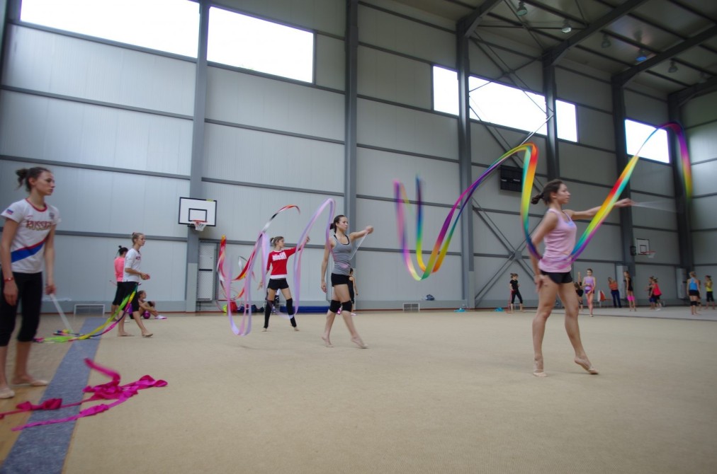 Athletes practicing rhythmic gymnastics with ribbons in an indoor hall during a training camp session
