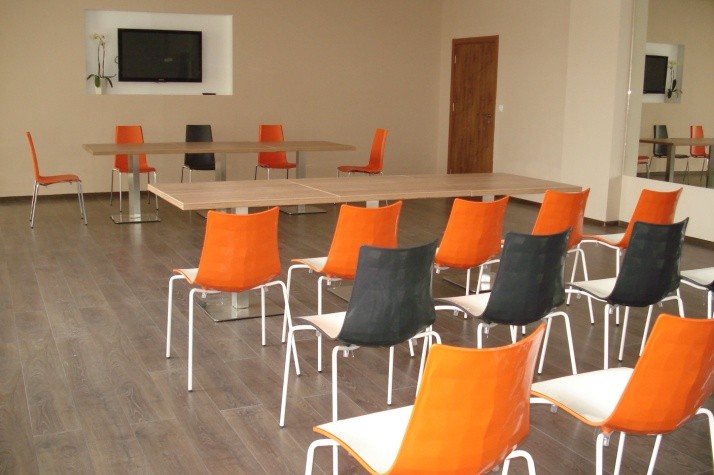 Conference room with orange and black chairs facing a screen, arranged for training camp presentations