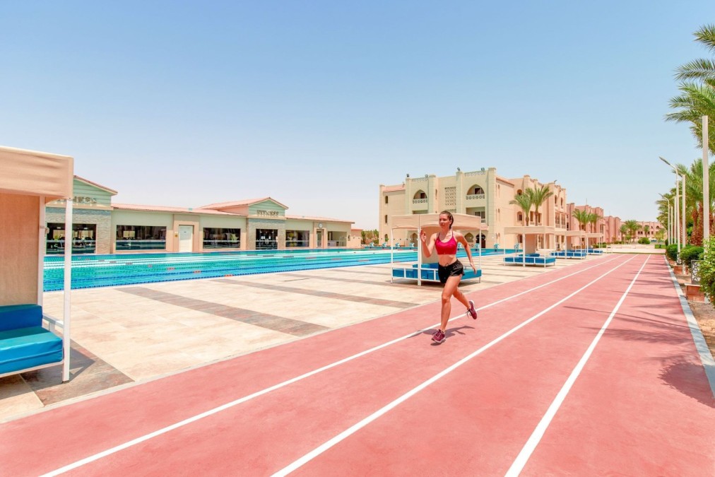 Runner training on red track alongside Olympic swimming pool