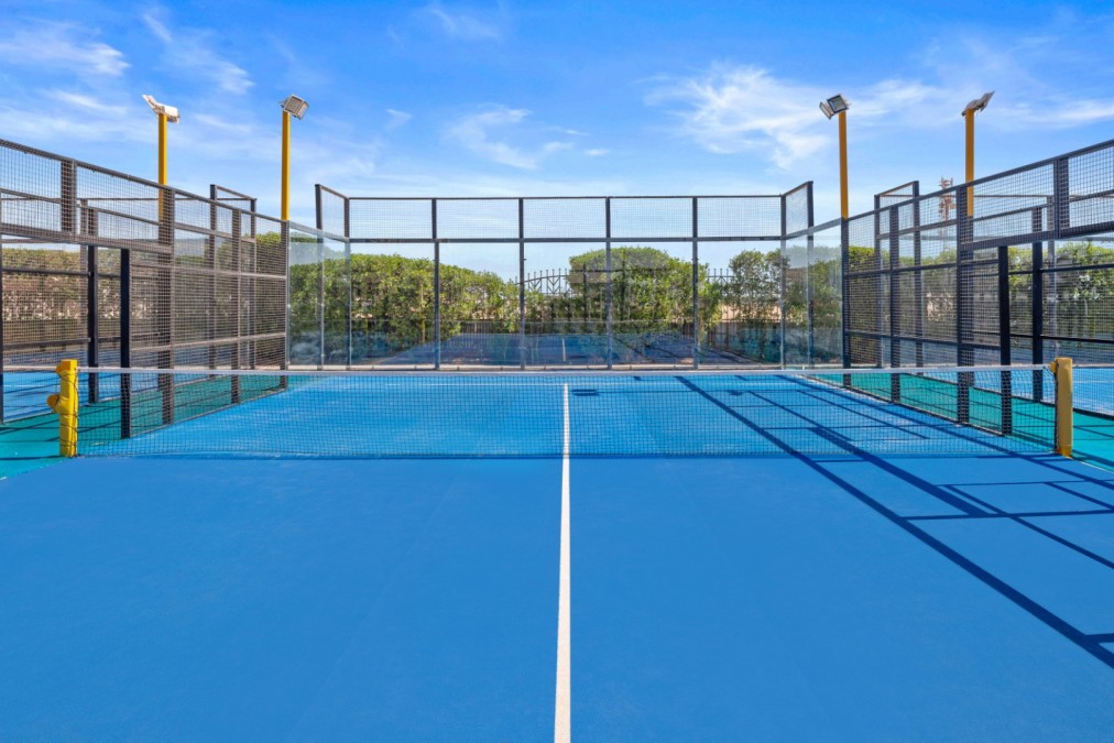 Front view of fenced padel tennis court with blue surface and lights