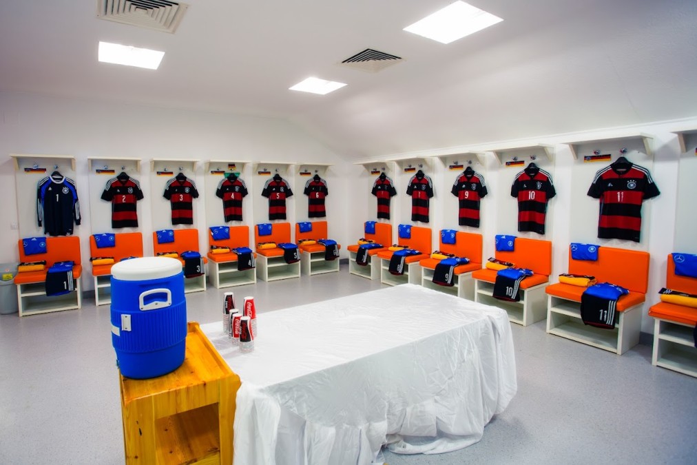 Football team locker room with numbered jerseys, benches and a hydration station.