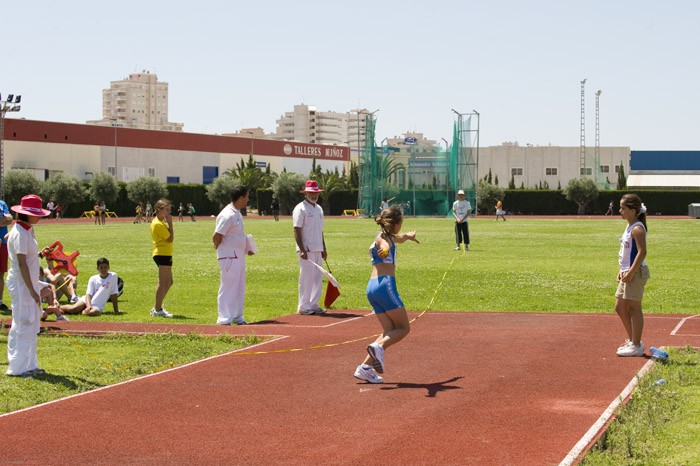 Athlete performing a jump into sand pit with officials on the track infield.