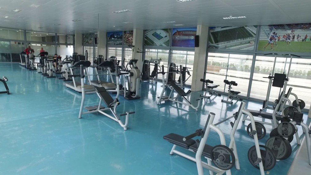 Fitness gym with cardio and strength machines, mirrors, and large windows.