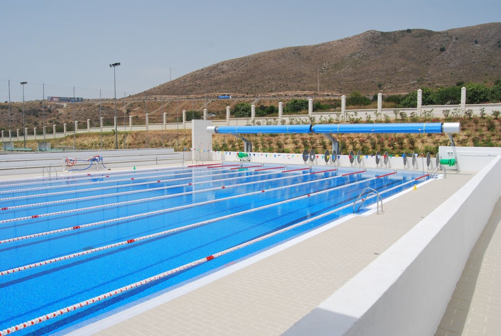 Outdoor lane pool with deck space, lane markers and a hillside backdrop.