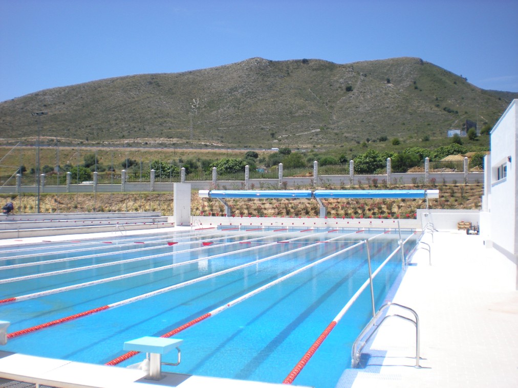 Side view of an outdoor swimming pool with marked lanes and mountain backdrop.