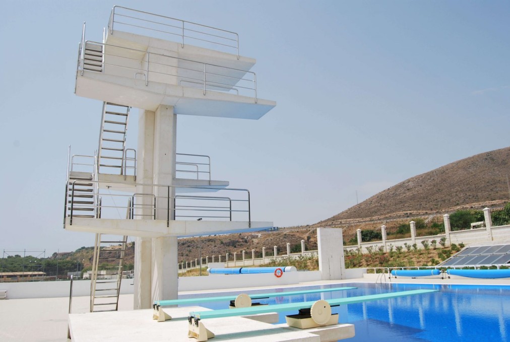 Diving platforms beside an outdoor pool with starting blocks and a hillside backdrop.