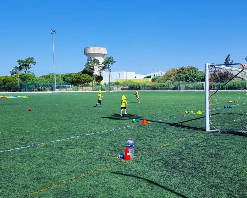 Children training on an outdoor football pitch with cones and small goals.