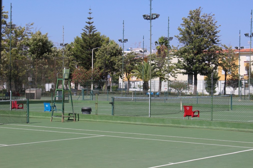 Several outdoor hard tennis courts with umpire chairs and floodlights.