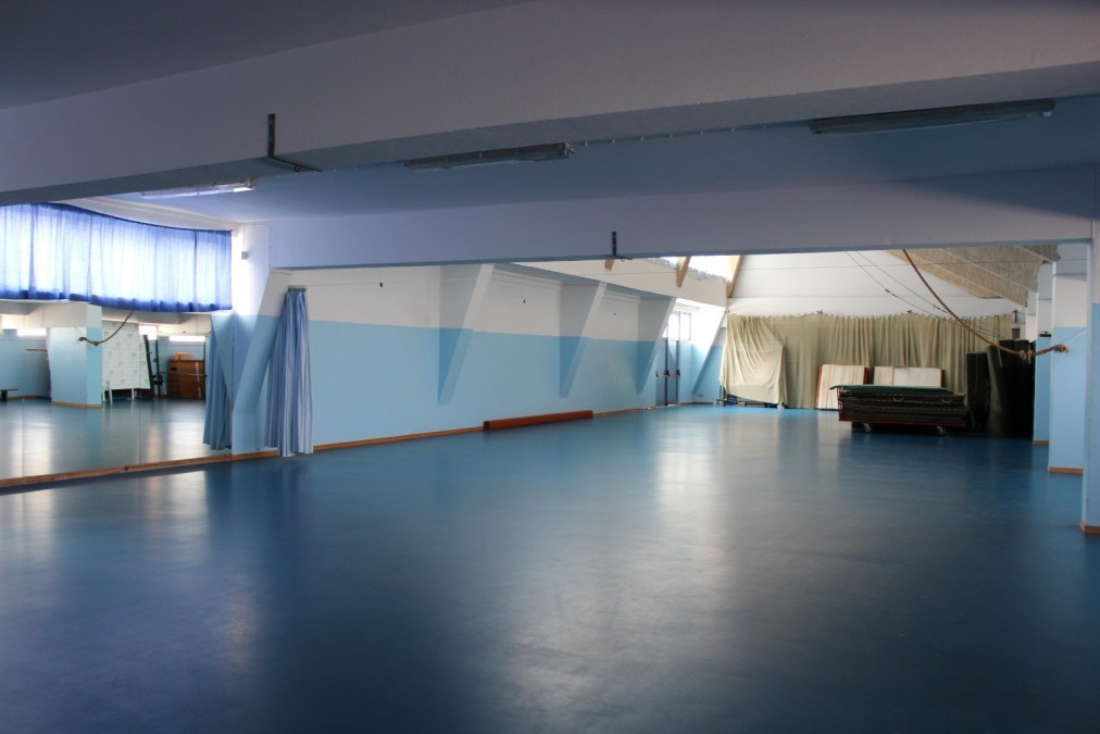 Large mirrored studio room with open floor space and stacked mats.
