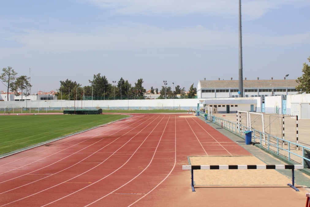 Outdoor running track with grass infield and a hurdles area.