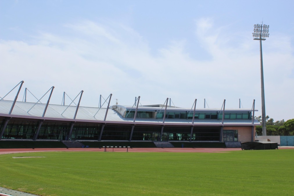 Modern athletics building beside a grass field and running track.