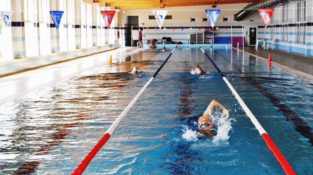 Athletes swim freestyle laps in an indoor training pool with marked lanes.