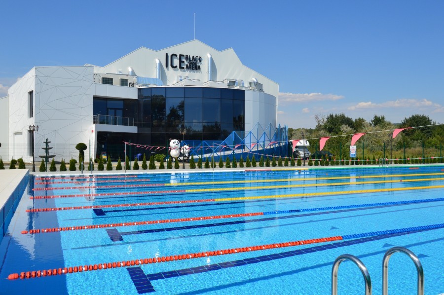 Outdoor pool with lane ropes, ice rink building beyond