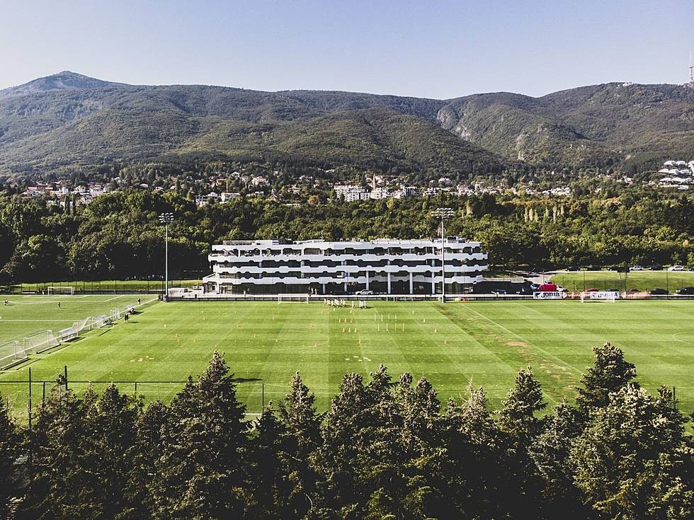 Soccer training complex with large grass pitch and accommodation building against mountain backdrop