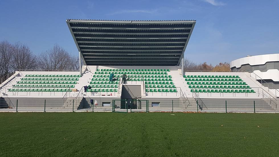 Small stadium stand with green seats facing a grass pitch, used for coaching observation during training camp