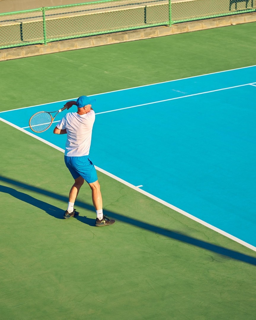 Athlete in white and blue outfit practicing tennis swing on outdoor court