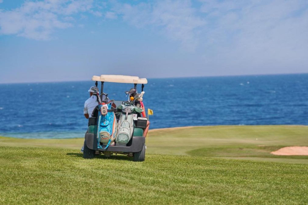 Golf cart with two bags on a seaside fairway, blue ocean and cloudy sky in the background