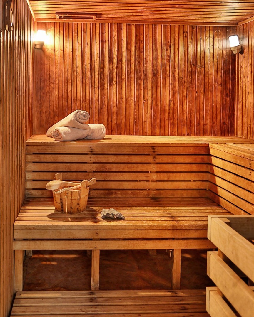 Wooden sauna room with benches, bucket, and towel for post-training relaxation