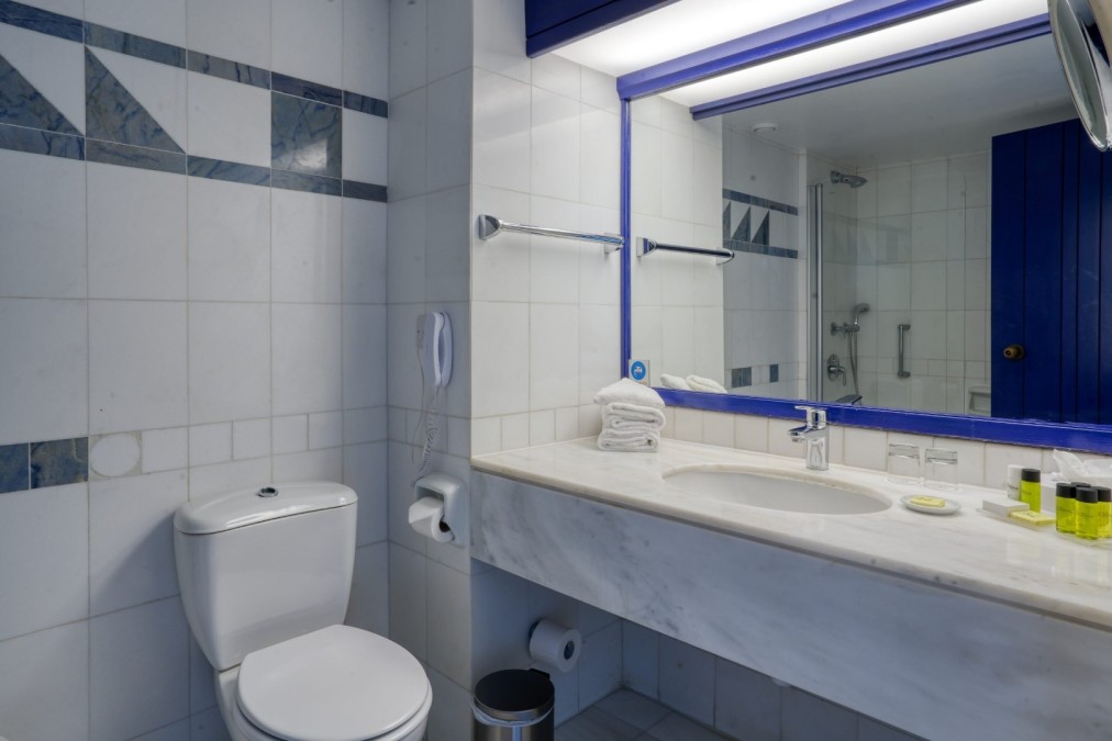 White-tiled bathroom with mirror, sink, and modern fixtures prepared for guests