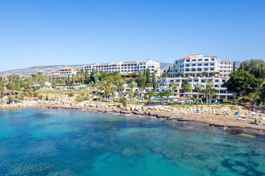 Seaside hotel complex with white buildings and palm trees overlooking a clear blue coastline