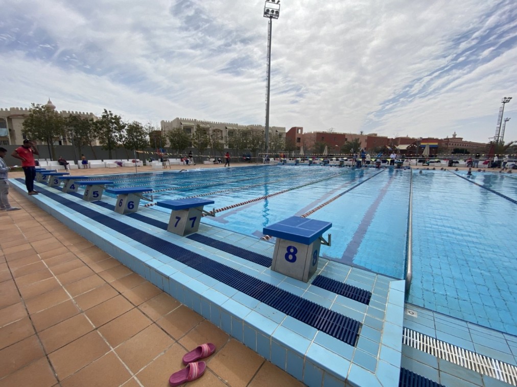 Outdoor 50m swimming pool with diving blocks, marked lanes, and surrounding seating