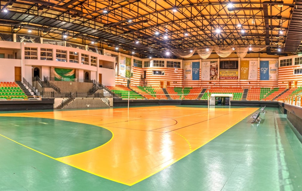 Indoor volleyball hall with wooden court, tiered seating and truss roof lighting
