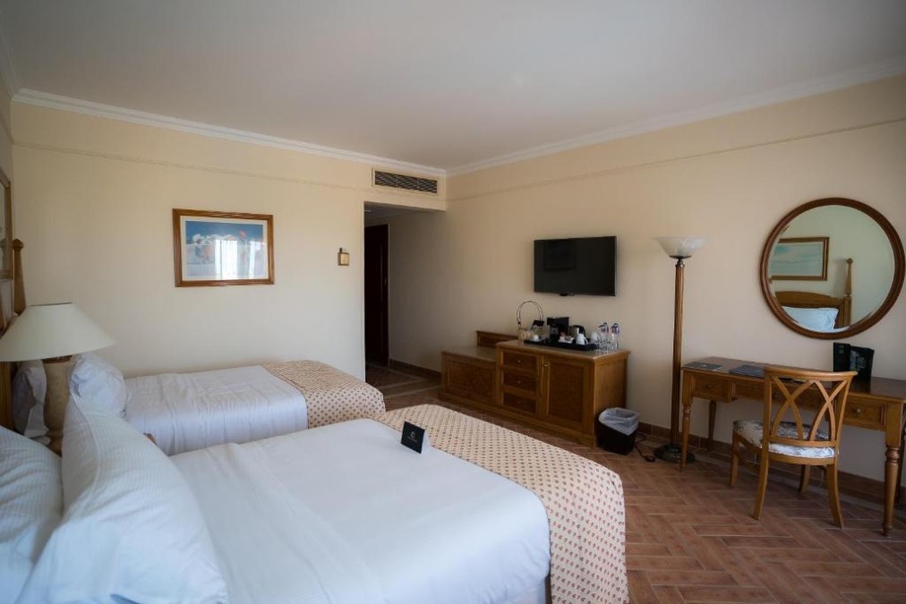Twin-bed hotel room with desk and TV, training camp accommodation for athletes