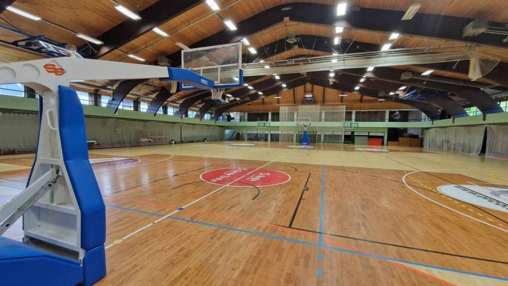 Large indoor sports hall with marked basketball court, wooden floor, and multiple hoops.