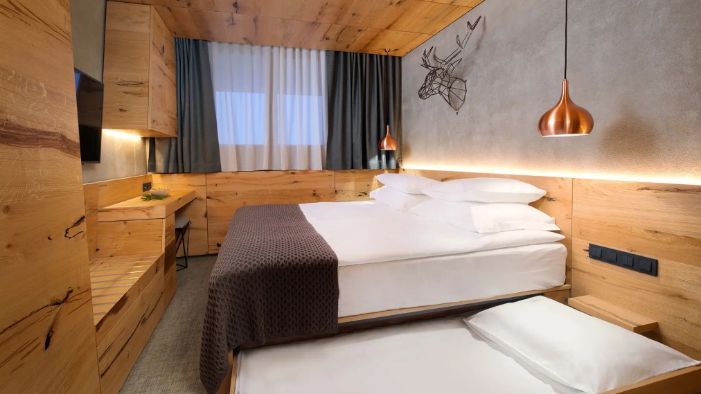 Modern wooden-accent hotel room with double bed, pull-out extra bed, and warm pendant lighting.