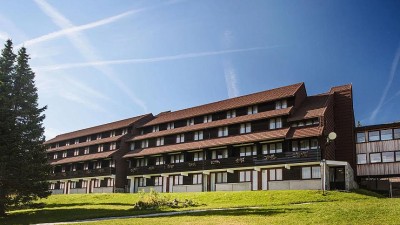 Exterior view of the hotel building with balconies, sloped roof, and surrounding green lawn.