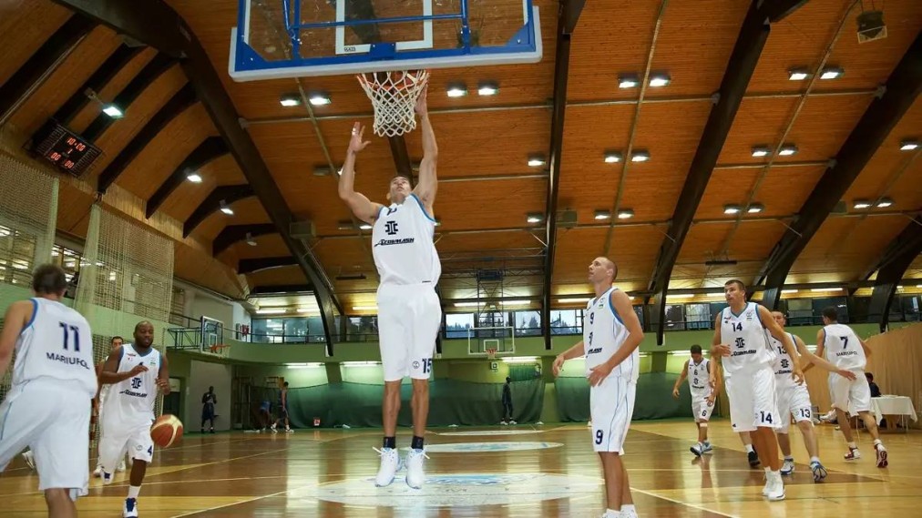 Basketball practice inside a large indoor sports hall with players warming up under the hoop.