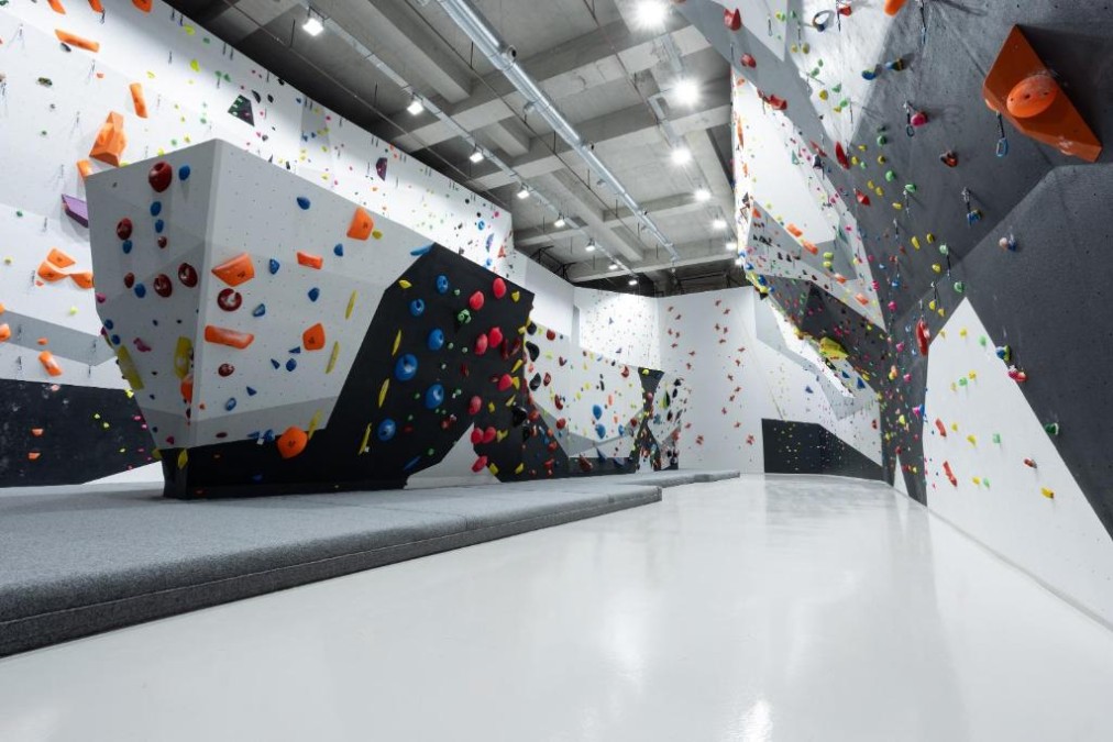 Large indoor bouldering hall with padded flooring and overhanging walls.