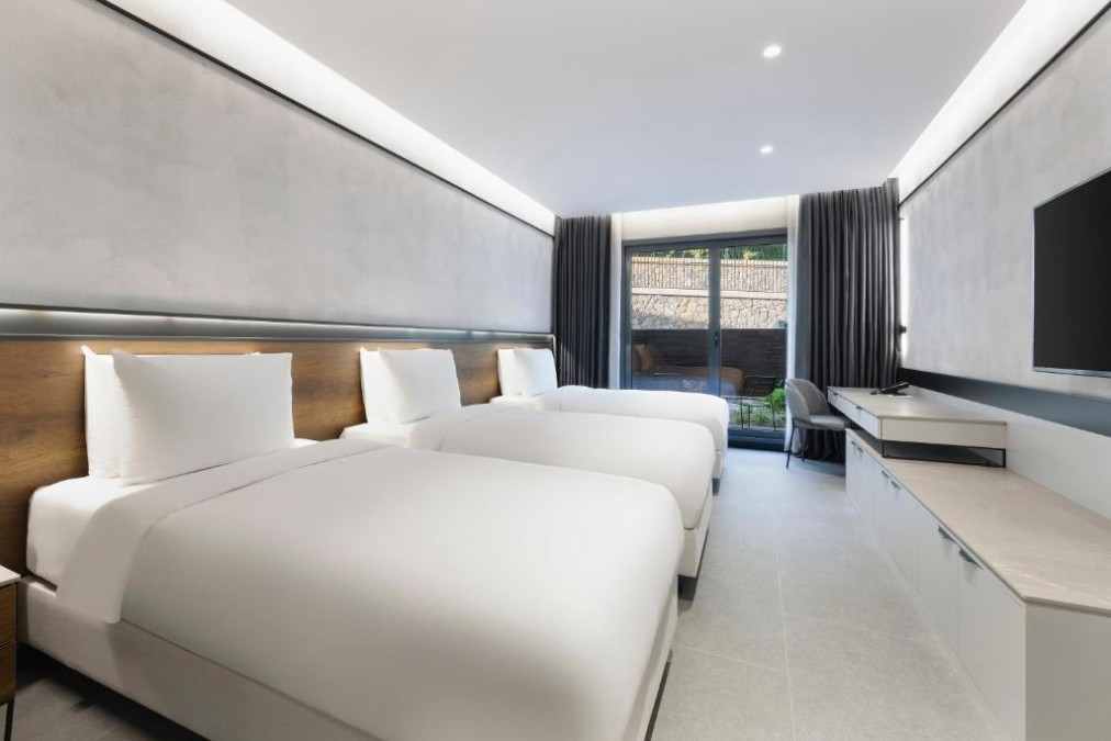 Bright triple room with three single beds, large TV, and balcony doors with blackout curtains.