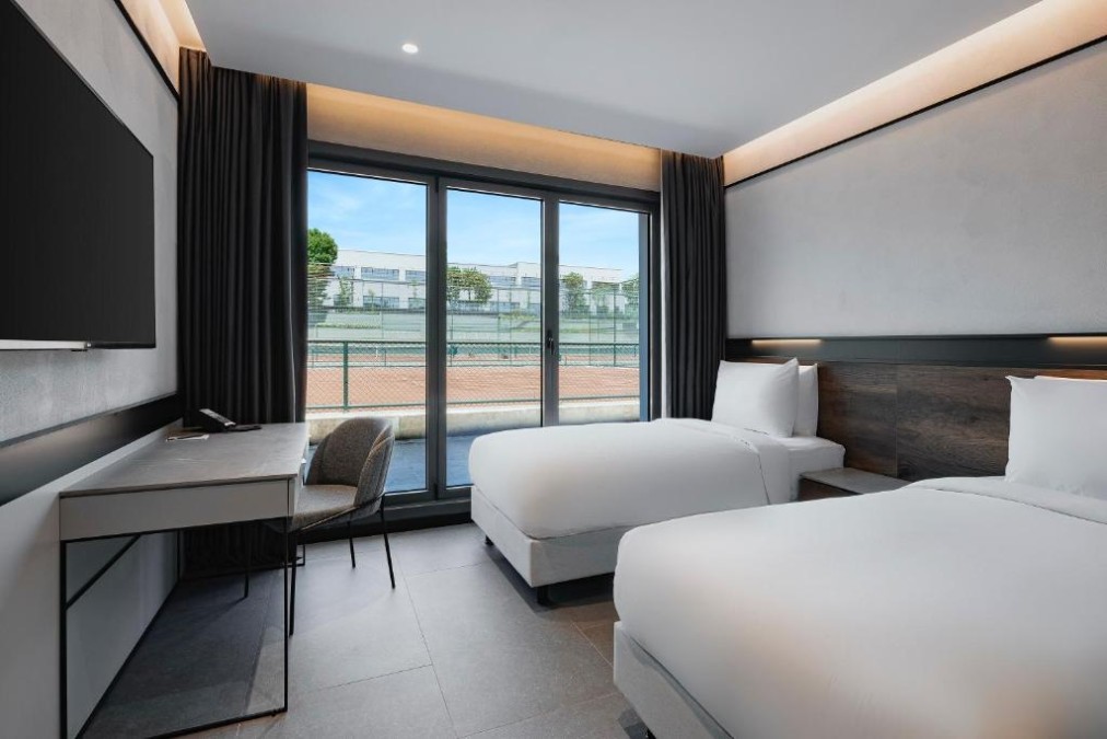 Twin room with balcony view over the tennis courts, featuring a desk and minimalist design.