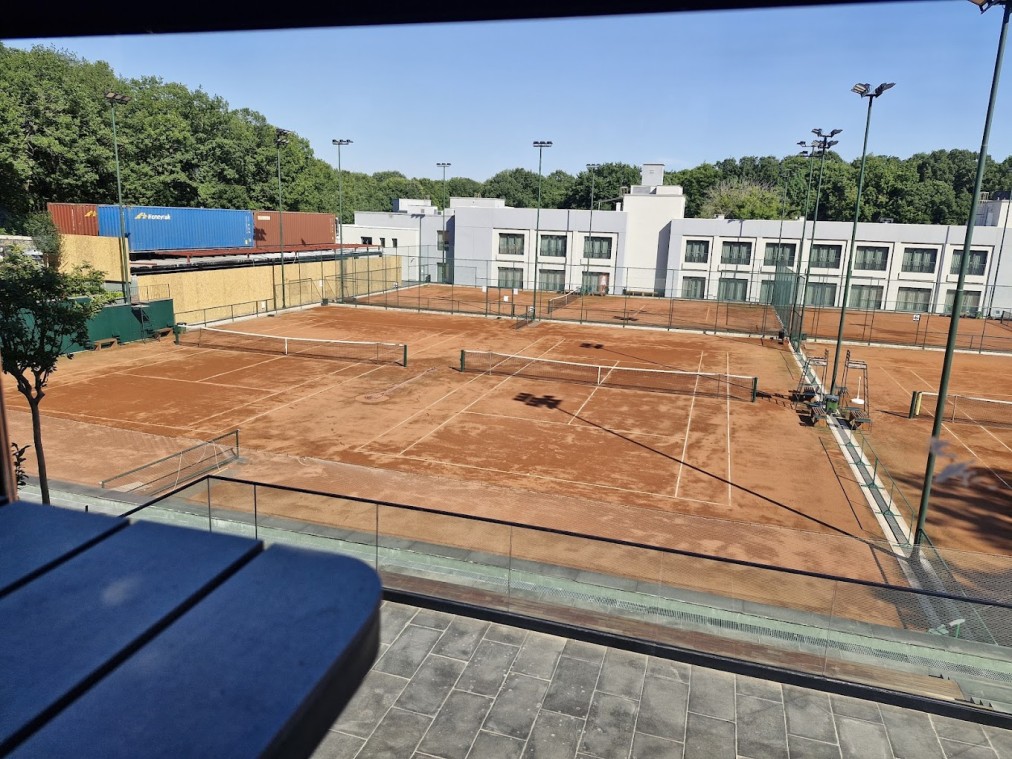 Outdoor clay tennis courts with fencing and floodlights beside the hotel building.