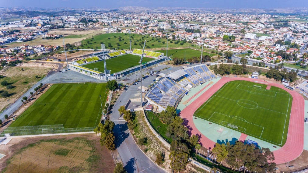 Aerial view of stadium, pitches and sports buildings beside the road.