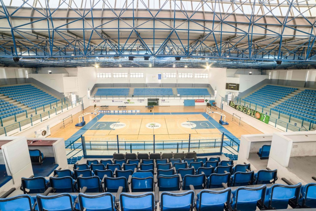 Indoor sports arena with court markings, hoops and blue seating.